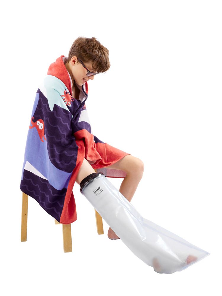 Beenbeschermer voor gips. Transparante hoes, zwarte afsluiting. Kind zit op kruk, been beschermd. CE-markering zichtbaar.