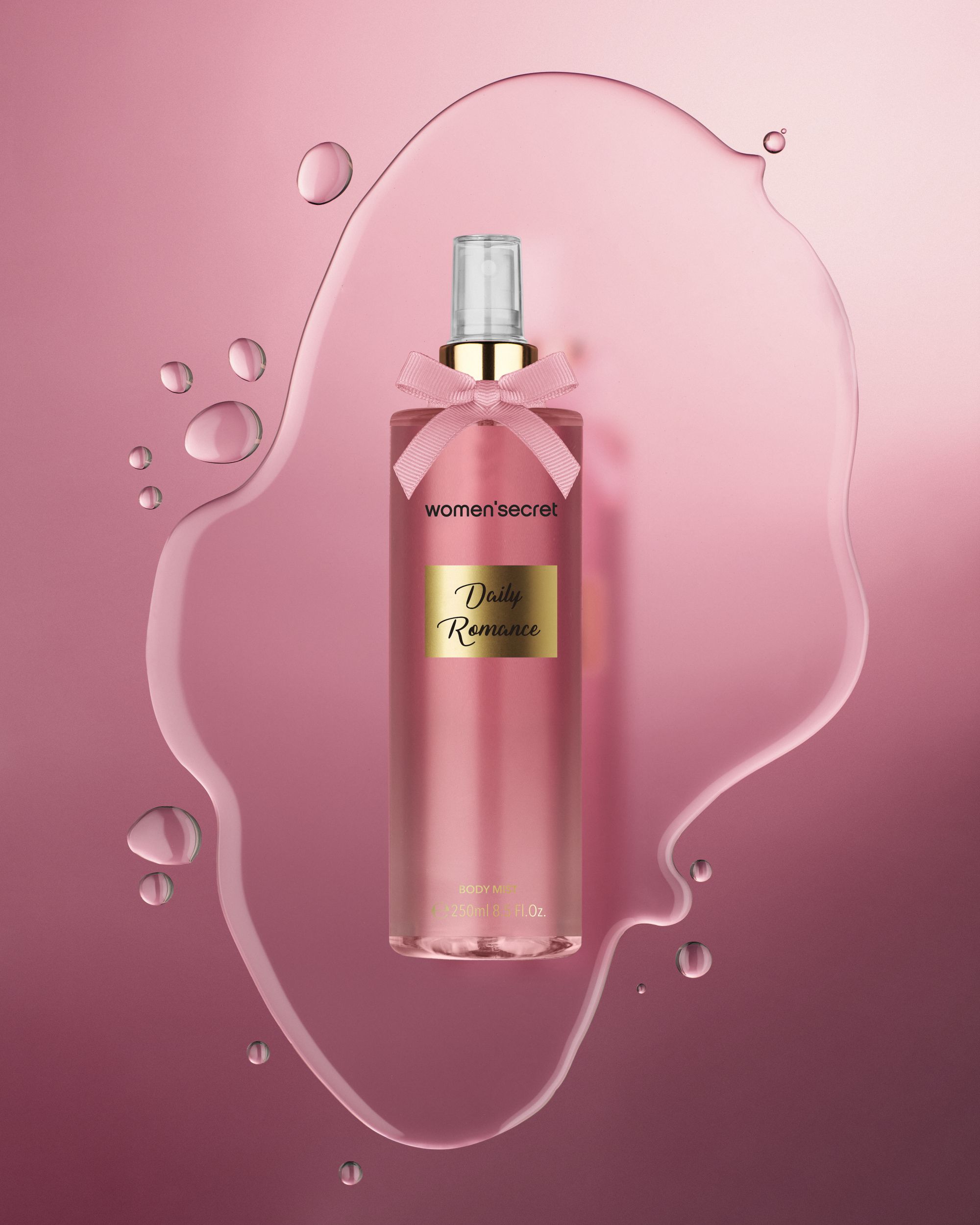 Flacon de brume corporelle rose avec nœud rose, entouré d'eau. Inscription 'women'secret' et 'Daily Romance'.