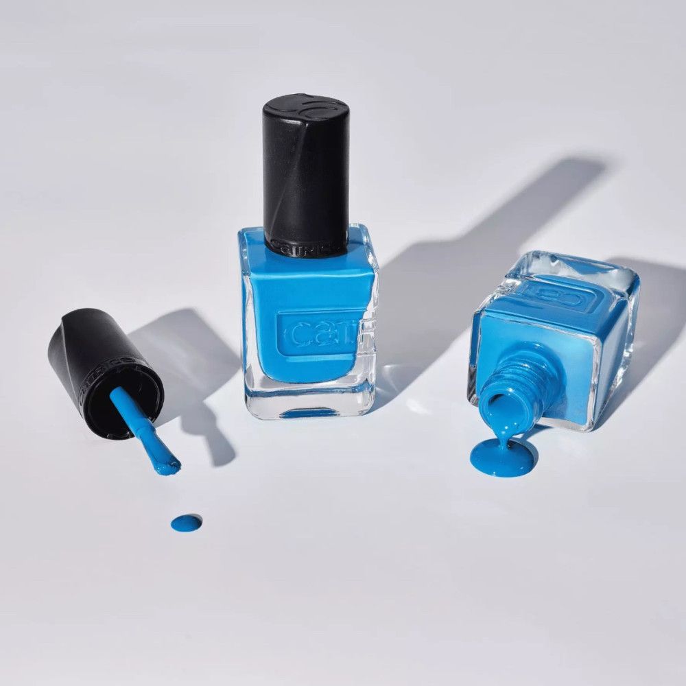 Trois flacons de vernis à ongles, un avec le bouchon ouvert, un renversé avec du vernis qui coule. "Catrice" est écrit sur les flacons.