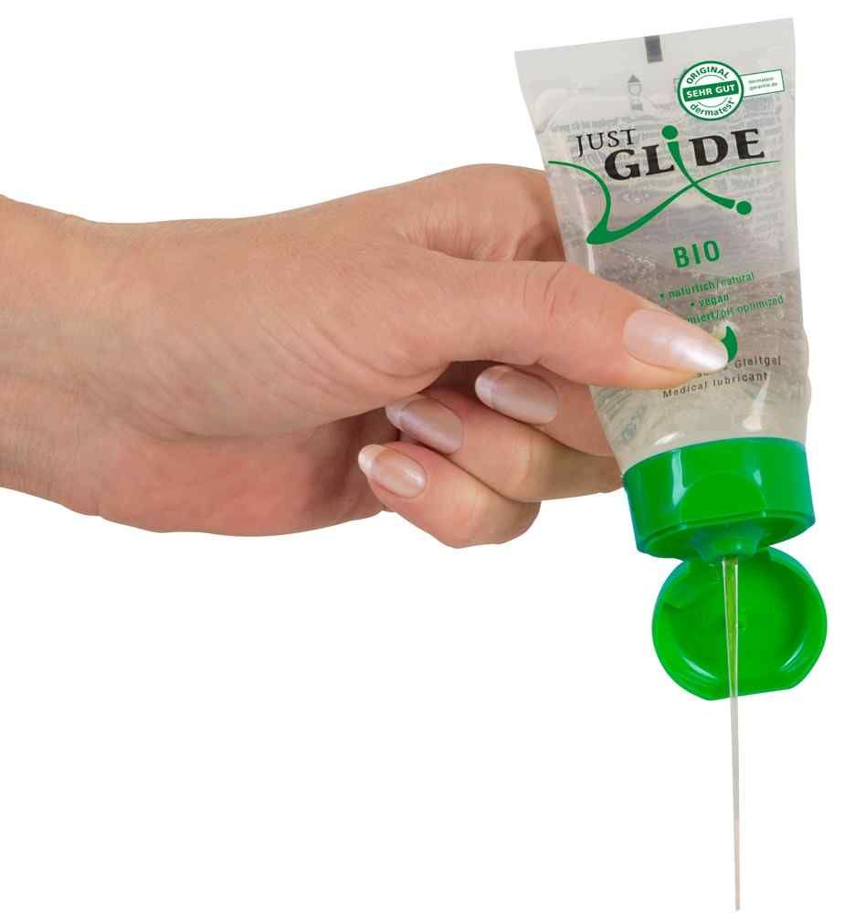 Hand houdt tube vast. Gel komt uit opening. Groene dop. Product: Just Glide Bio. Transparante gel.