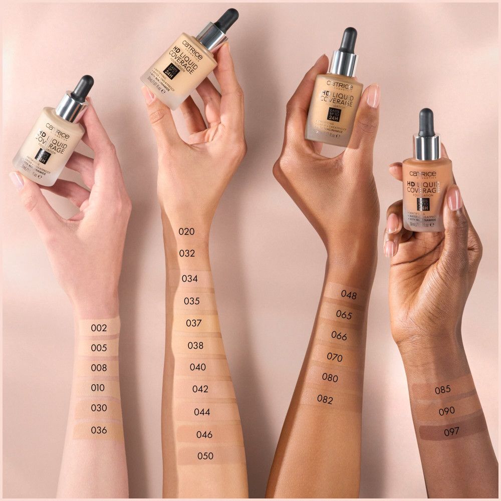 Mains tenant des flacons de fond de teint de différentes teintes. Numéros de couleurs sur les bras. Catrice HD.