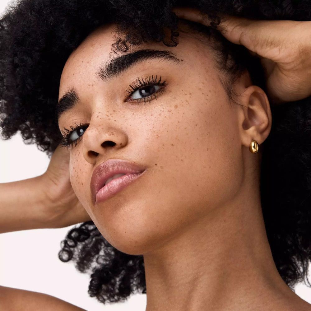 Gros plan d'un visage avec des cils maquillés. La peau est couverte de taches de rousseur.