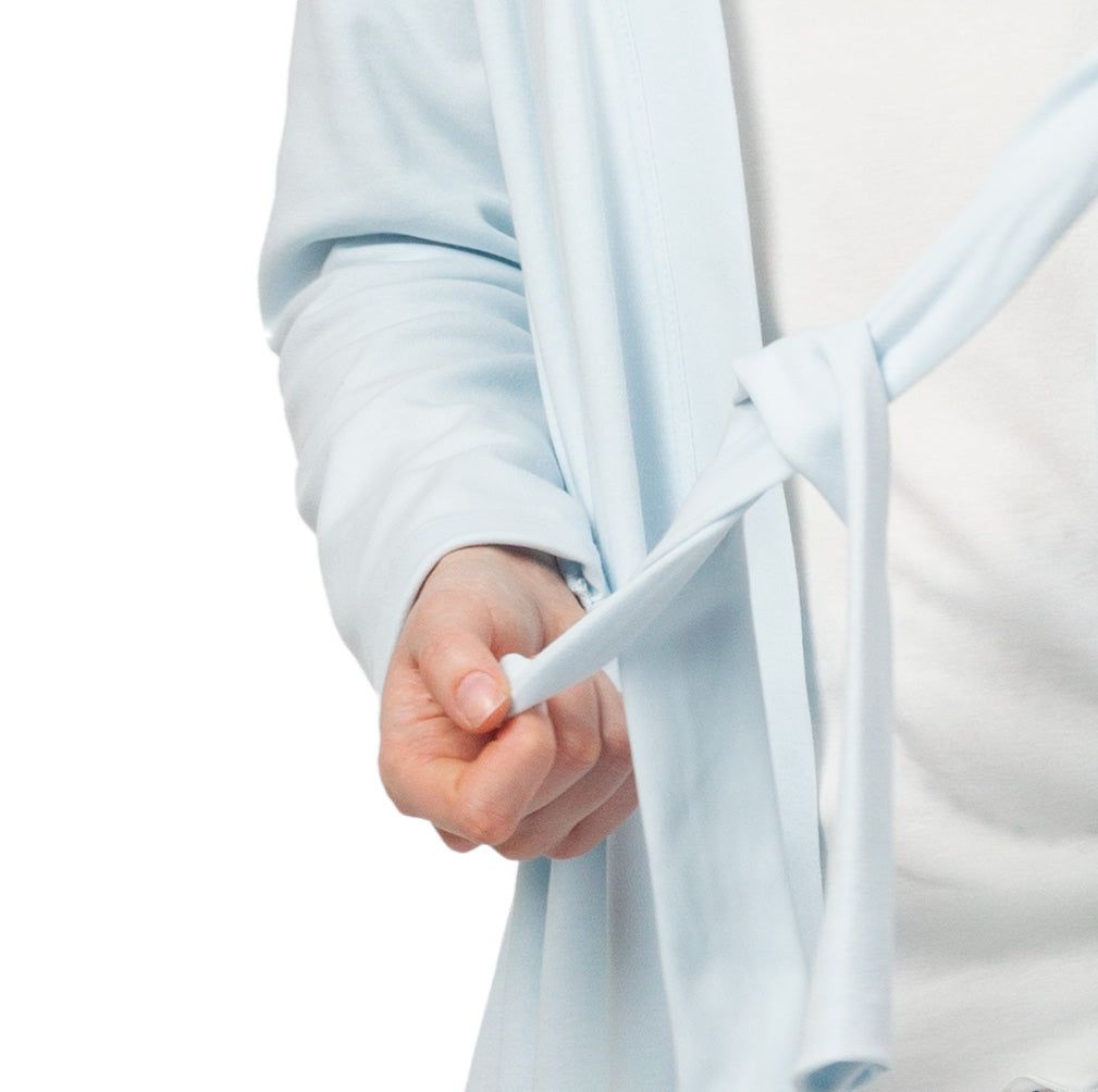 Close-up: Lichtblauwe katoenen ochtendjas met strikceintuur. Persoon knoopt de ceintuur.