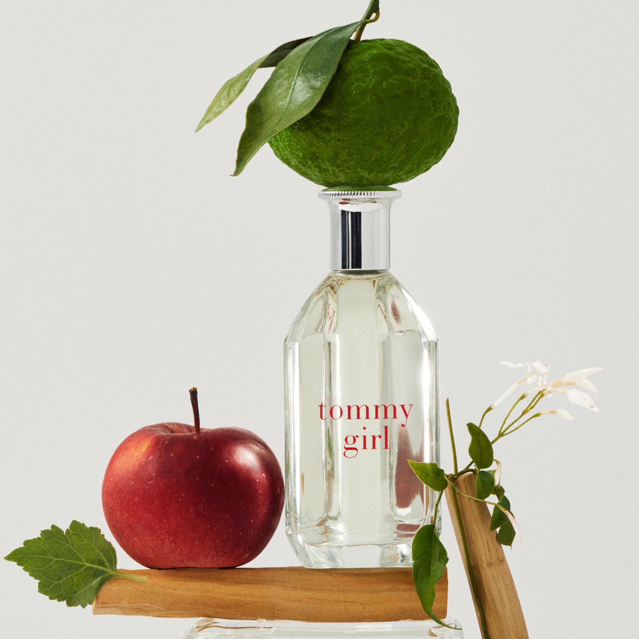 Fles met zilveren dop, opschrift "tommy girl". Decoratie met appel, citroen en bloemen. Geplaatst op stukken hout.