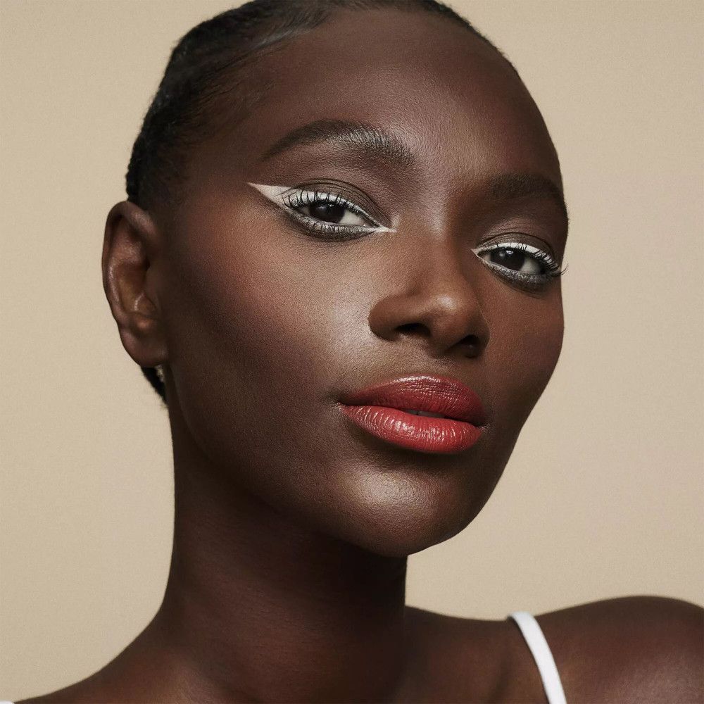Femme à la peau foncée avec trait de khôl blanc sur la paupière supérieure et rouge à lèvres rouge.