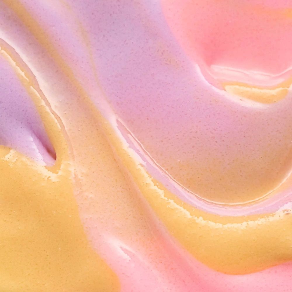 Gros plan sur un gommage pour les lèvres multicolore. Tourbillons roses, jaunes et violets. Texture brillante.