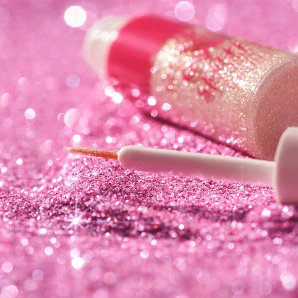 Close-up van een eyeliner-applicator op roze glitter. Flesje op de achtergrond.