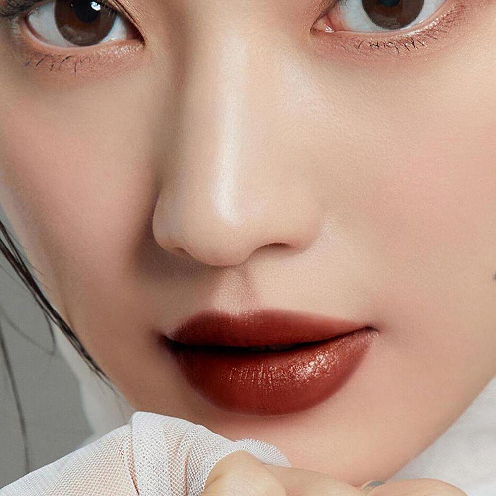 Close-up van lippen met donkerbruine lipgloss. De lippen zijn glanzend en vol. Lichte huidskleur.