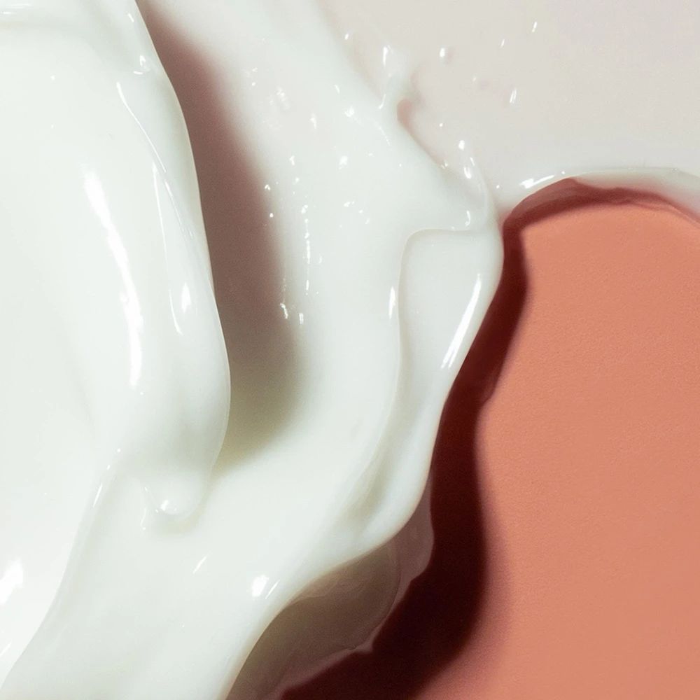 Gros plan de crème blanche sur fond rose. La crème a une texture lisse et brillante.