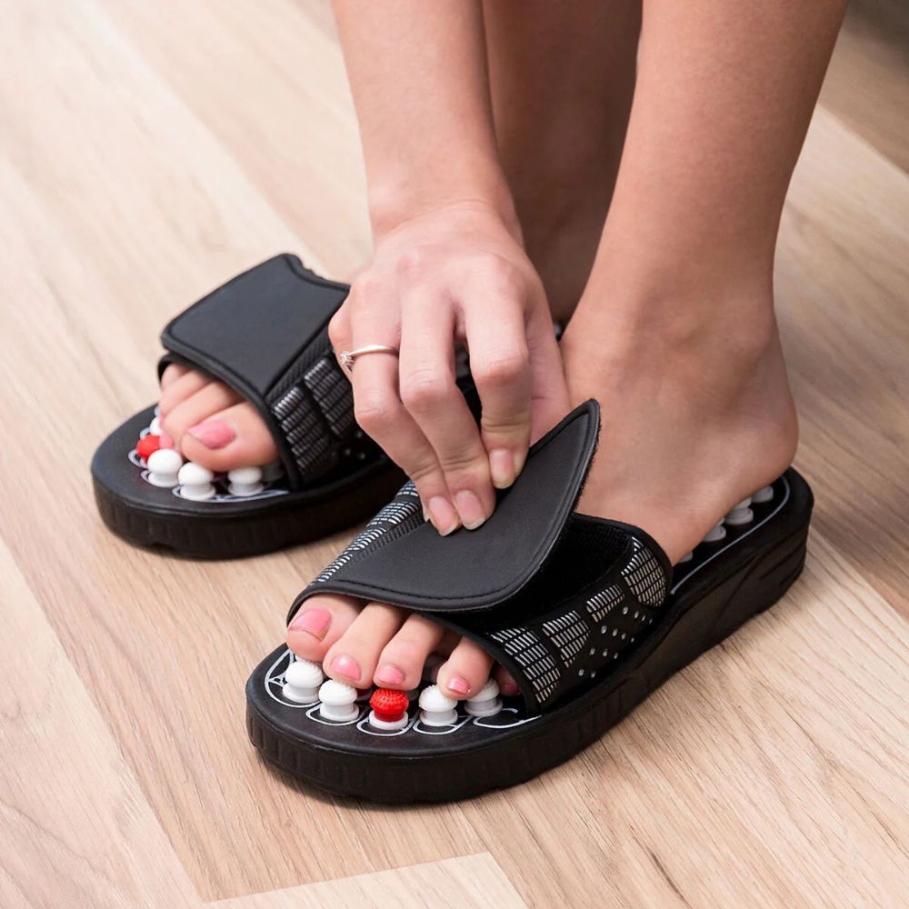 Persoon opent de riem van een acupressuurschoen. Zwarte schoenen met witte en rode noppen.
