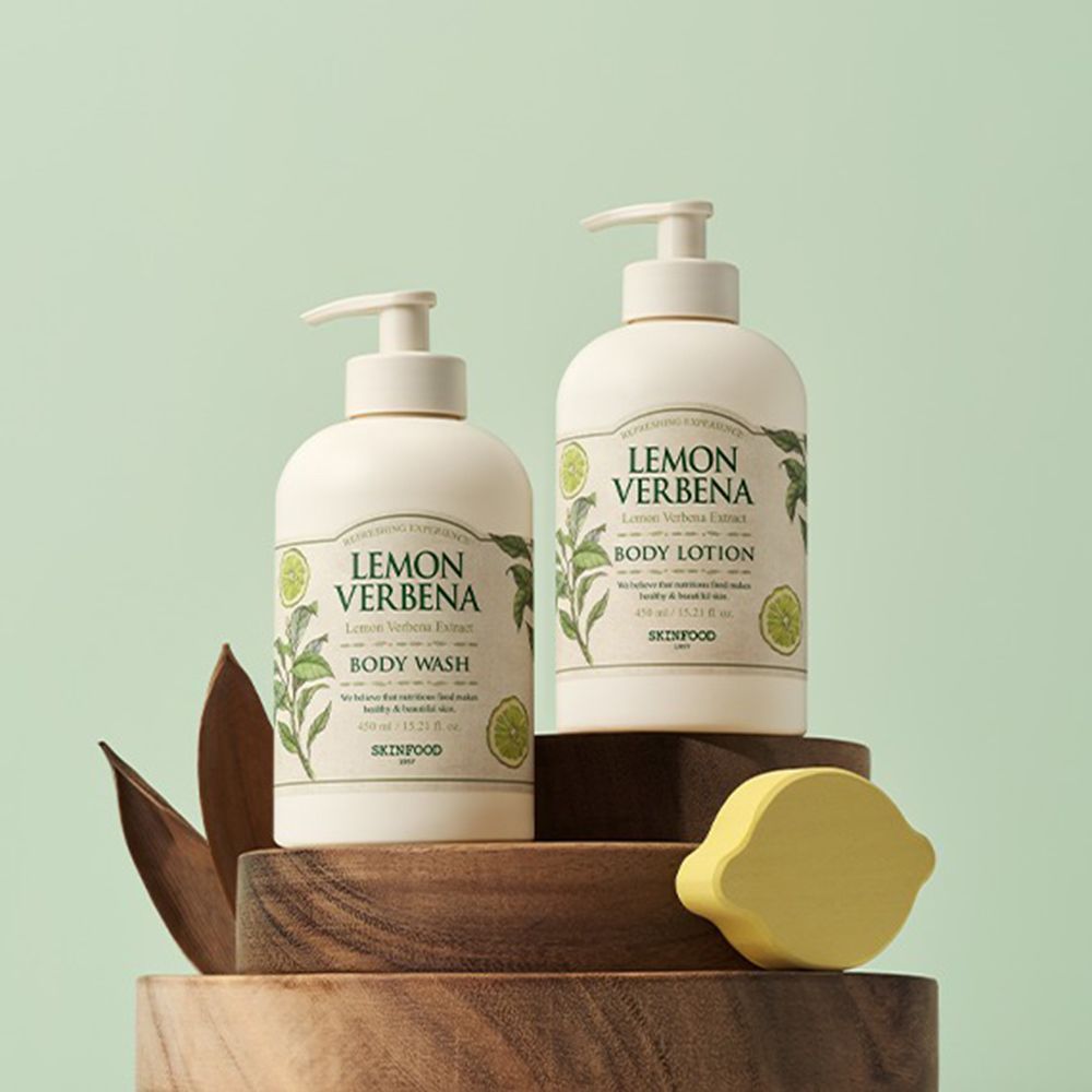 Deux flacons avec pompe. Inscription: Lemon Verbena Body Wash et Body Lotion. Sur socle en bois, fond vert.