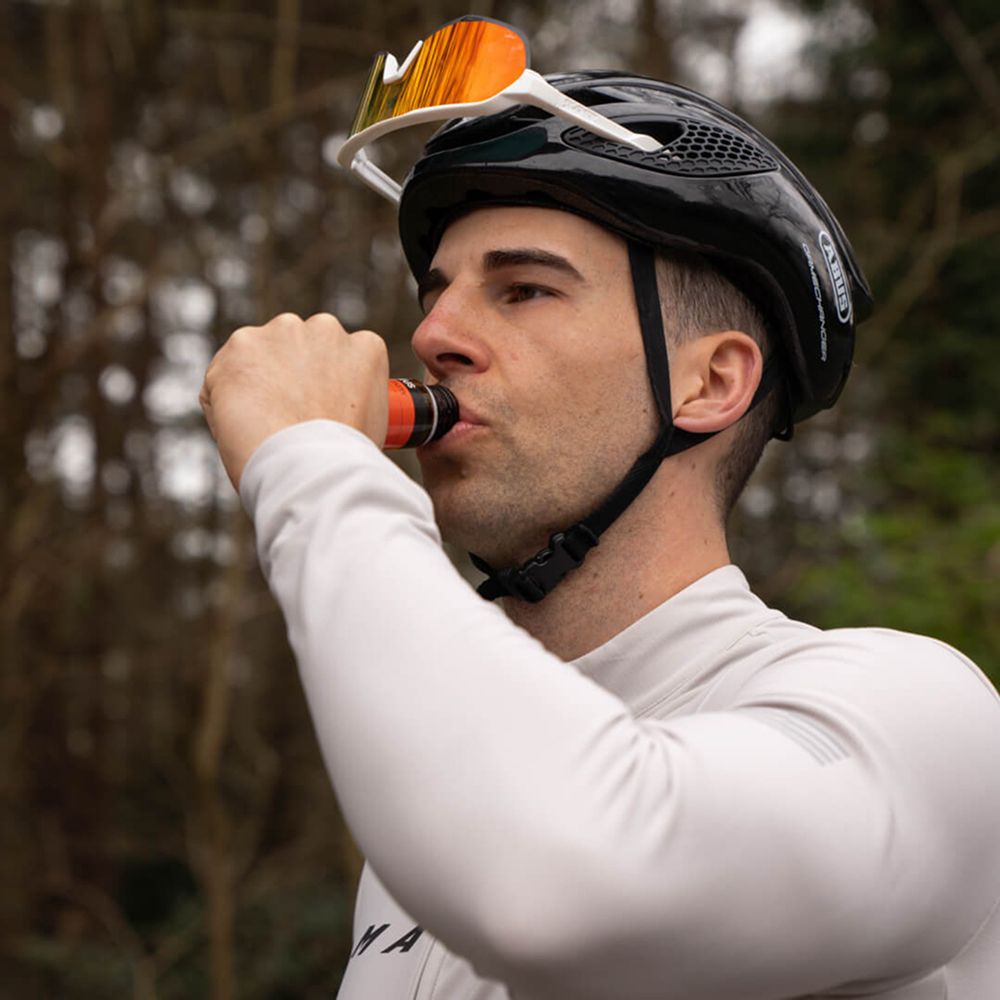 Homme buvant d'une bouteille. Il porte un casque et des lunettes de soleil. Arbres en arrière-plan.