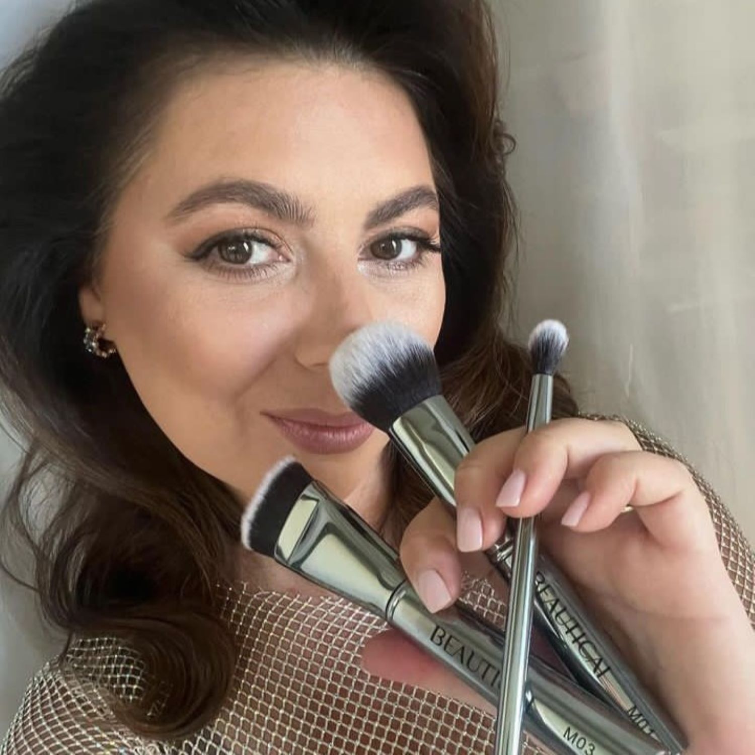 Femme tenant trois pinceaux. La marque BEAUTICAL est visible. Manches argentés.
