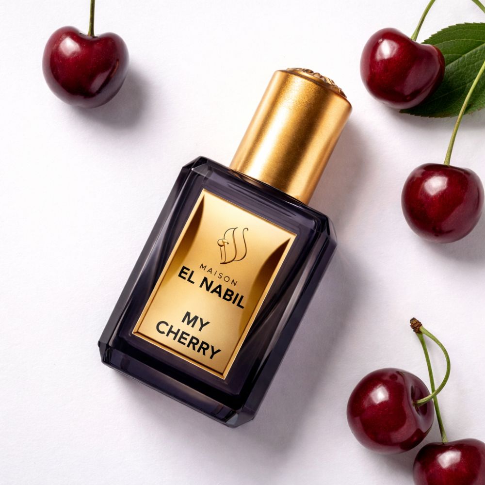 Flacon de parfum foncé avec bouchon et étiquette dorés. Des cerises entourent le flacon. Inscription : El Nabil, My Cherry.