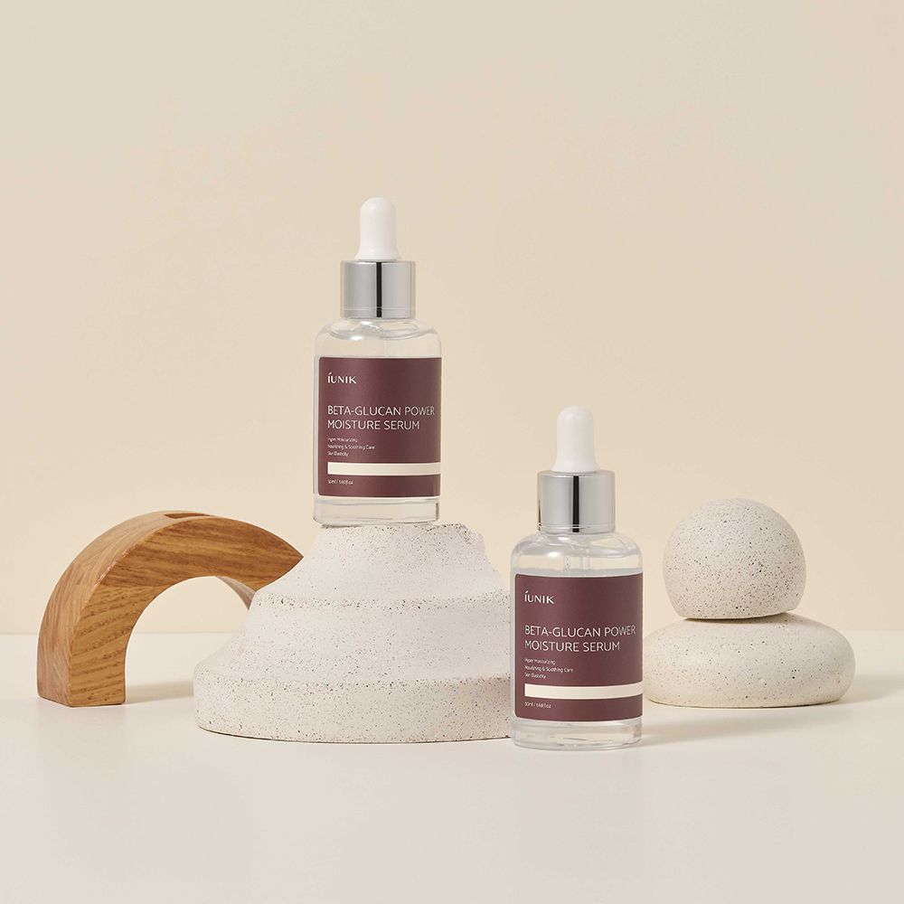 Deux flacons de sérum sur socle. Décoration en bois et pierre. Étiquette avec texte: iUNIK, Beta-Glucan Power Moisture Serum.