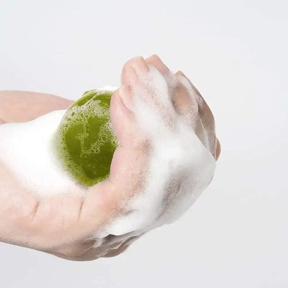 Groenachtige bal in hand, omgeven door schuim. Heldere, ronde vorm. Handen in focus.