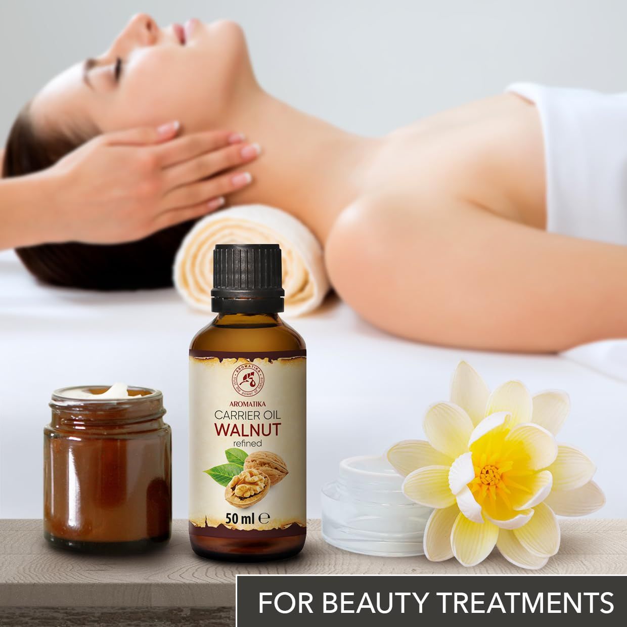 Flacon d'huile de noix AROMATIKA près de pots de massage et fleur, pour soins de beauté.