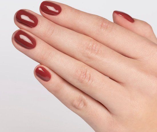 Main avec ongles vernis. Couleur : Burgundy Bliss. Finition brillante. Cinq ongles vernis.
