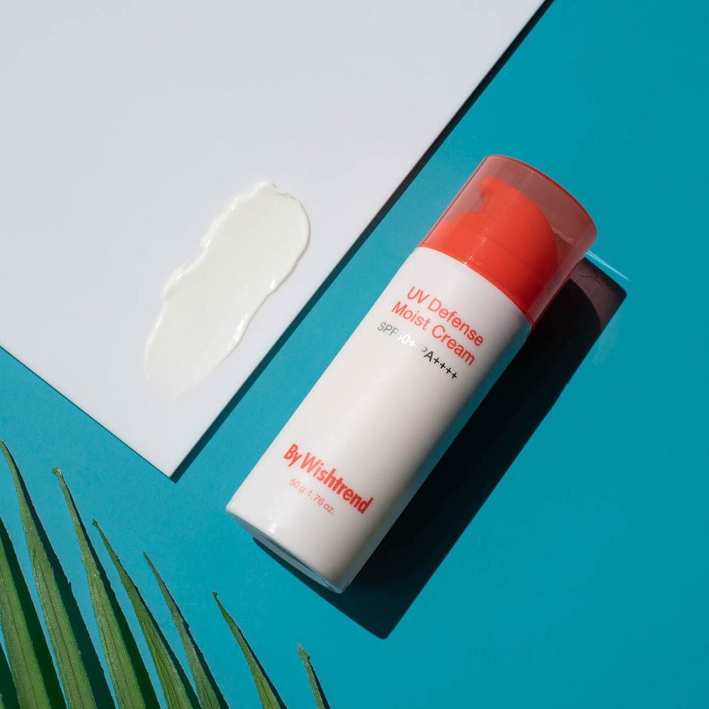 Witte tube met rode dop. Tekst: UV Defense Moist Cream SPF 50+ PA++++. Crème-monster. Op blauwe achtergrond.