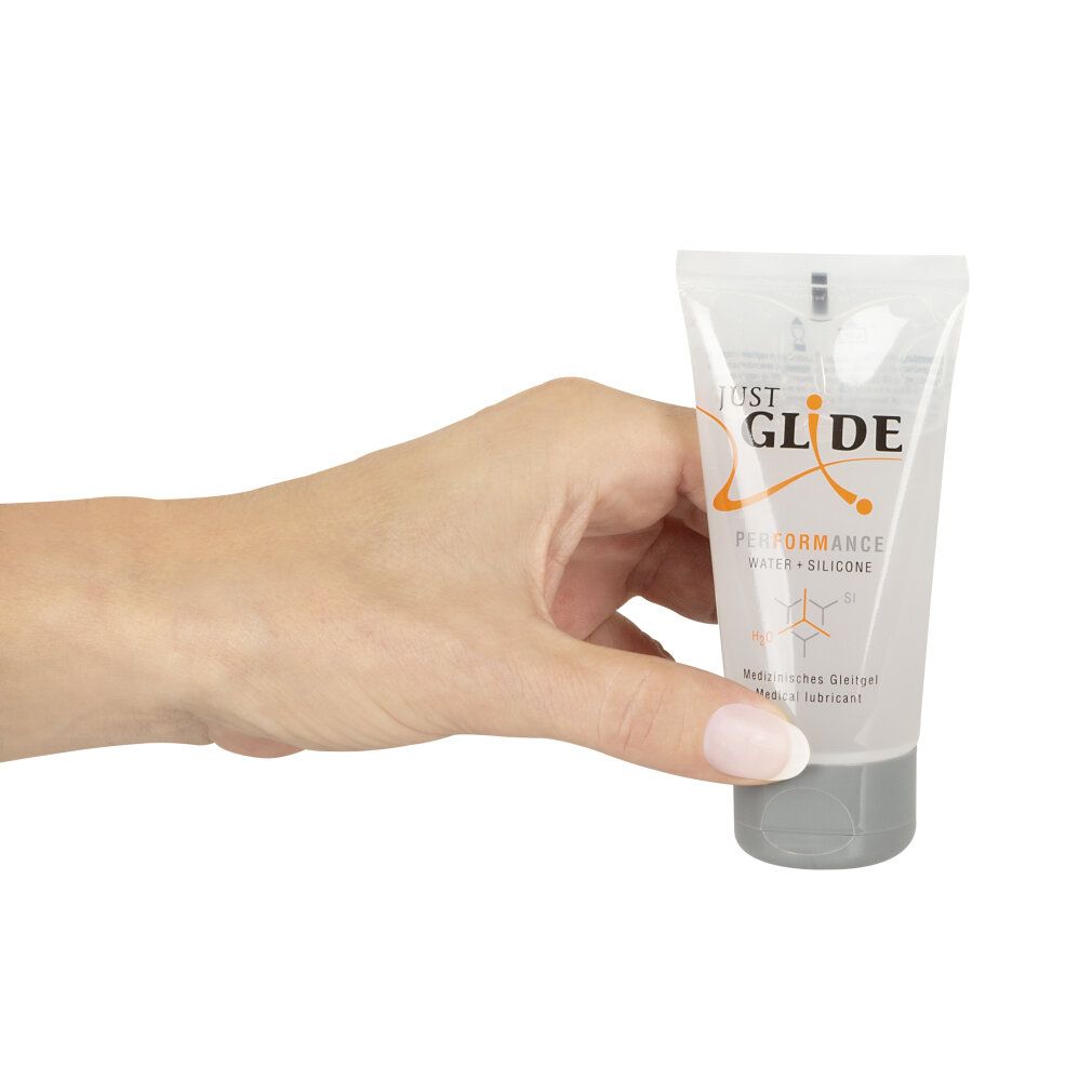 Main tenant un tube transparent avec bouchon gris. Inscription: JUST GLIDE PERFORMANCE WATER + SILICONE. Texte: Lubrifiant médical.