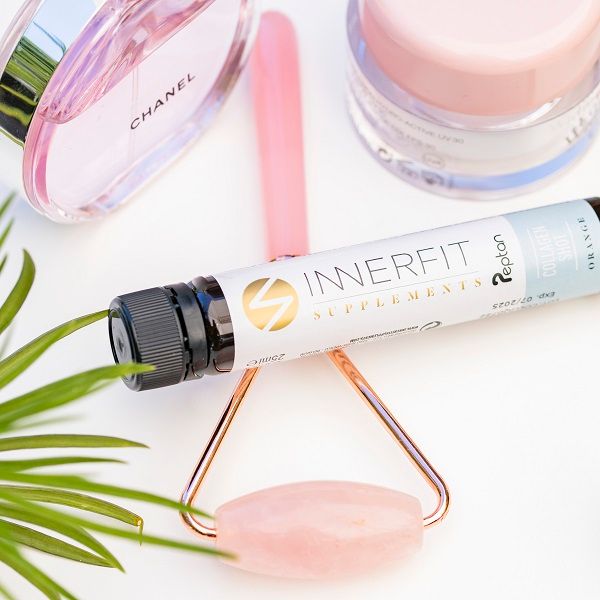 Ampoule en verre avec bouchon noir, à côté de produits cosmétiques et d'un rouleau facial. Inscription : Innerfit Supplements, Collagen Shot, Orange.