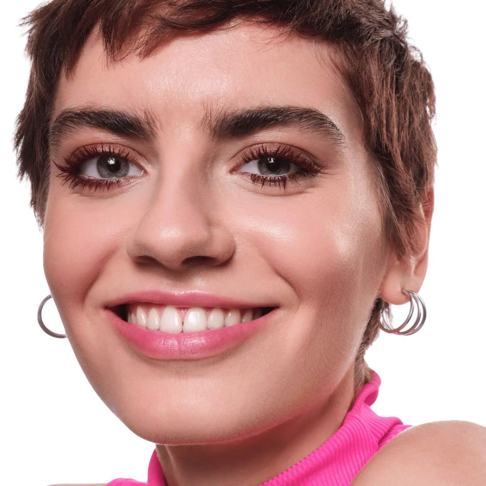 Portrait d'une femme aux cheveux courts bruns. Elle porte un col roulé rose et des boucles d'oreilles. Elle sourit.