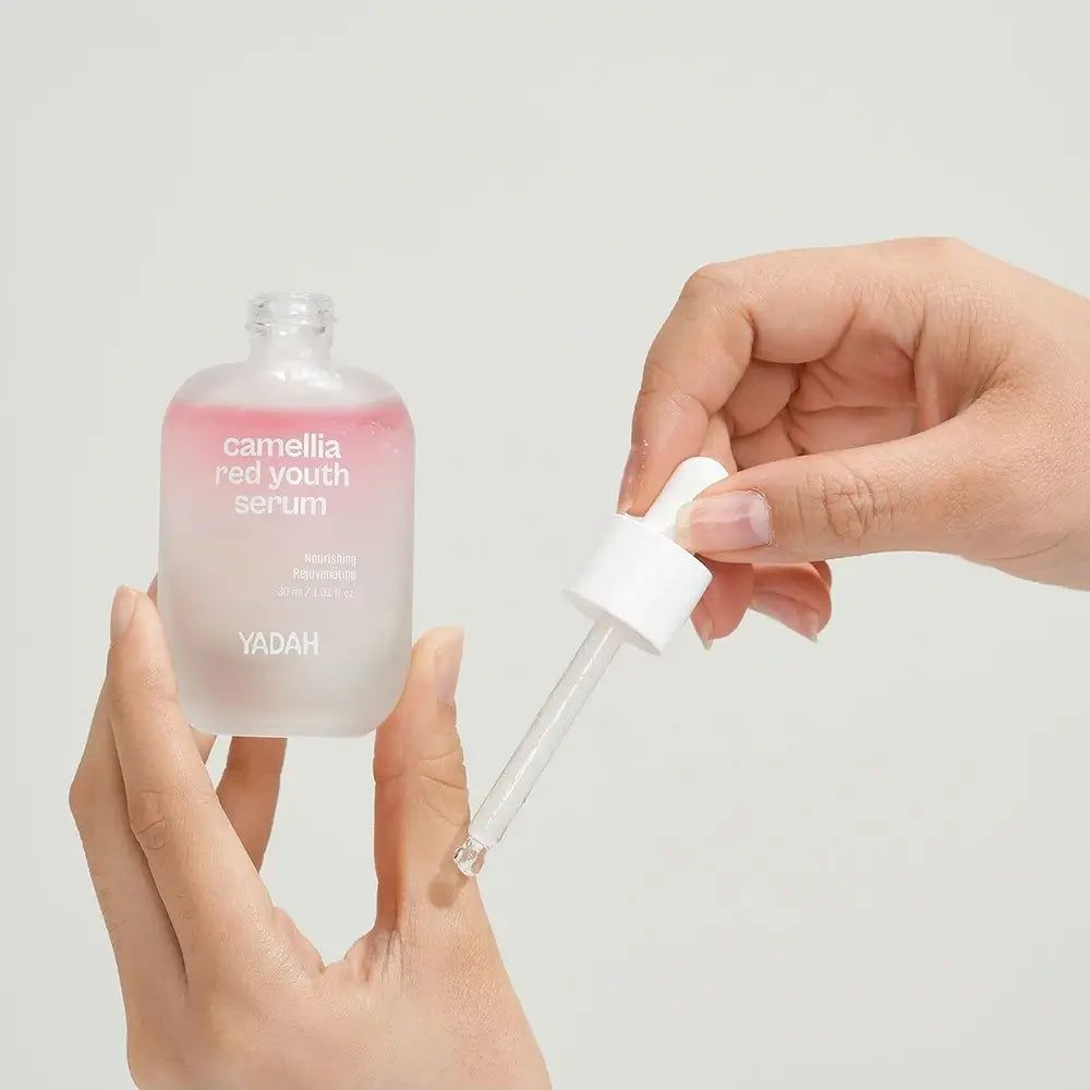 Serumfles met pipet. Opschrift: Camellia Red Youth Serum. Merk YADAH. Handen houden fles en pipet vast.