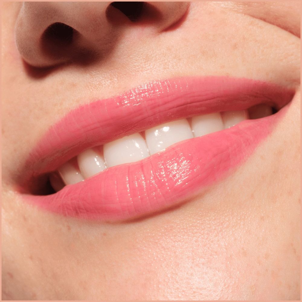 Gros plan sur des lèvres maquillées avec un plumper à lèvres rose. Dents visibles.