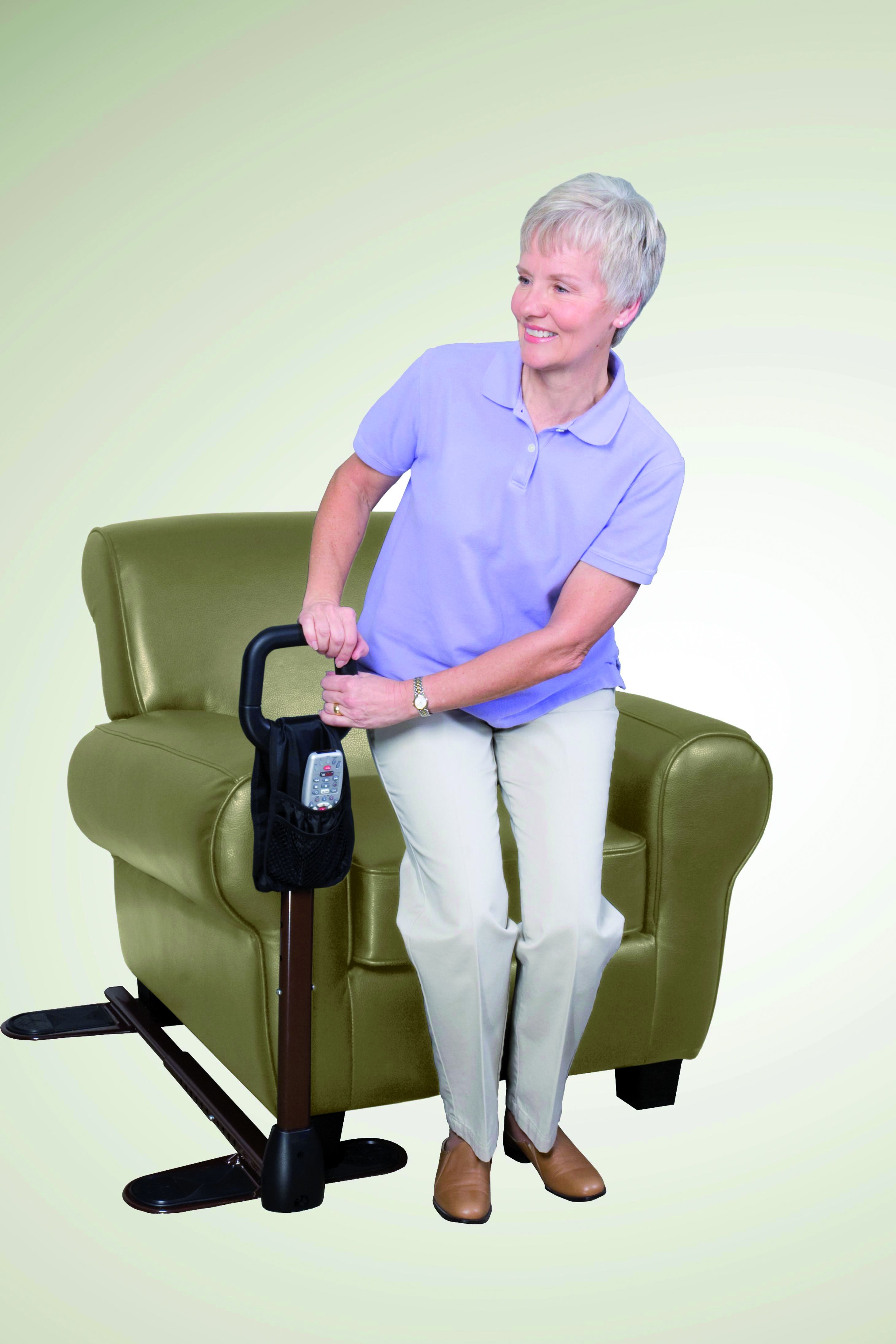 Femme utilisant une aide au lever près d'un fauteuil vert. Poignée noire, tige marron, base noire. Avec poche.