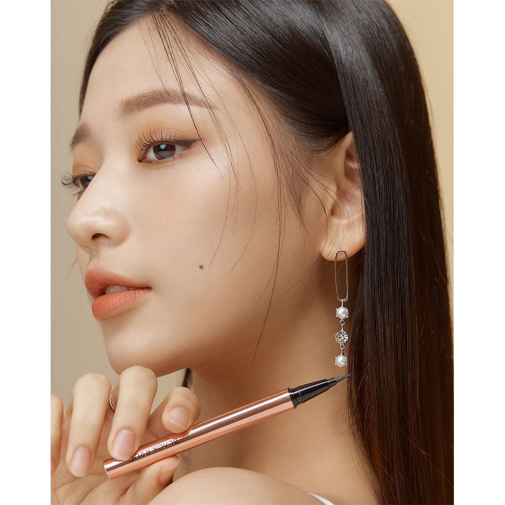 Een vrouw houdt een zwarte eyeliner pen vast. De pen heeft een roségouden behuizing. De vrouw heeft lang haar en draagt oorbellen.