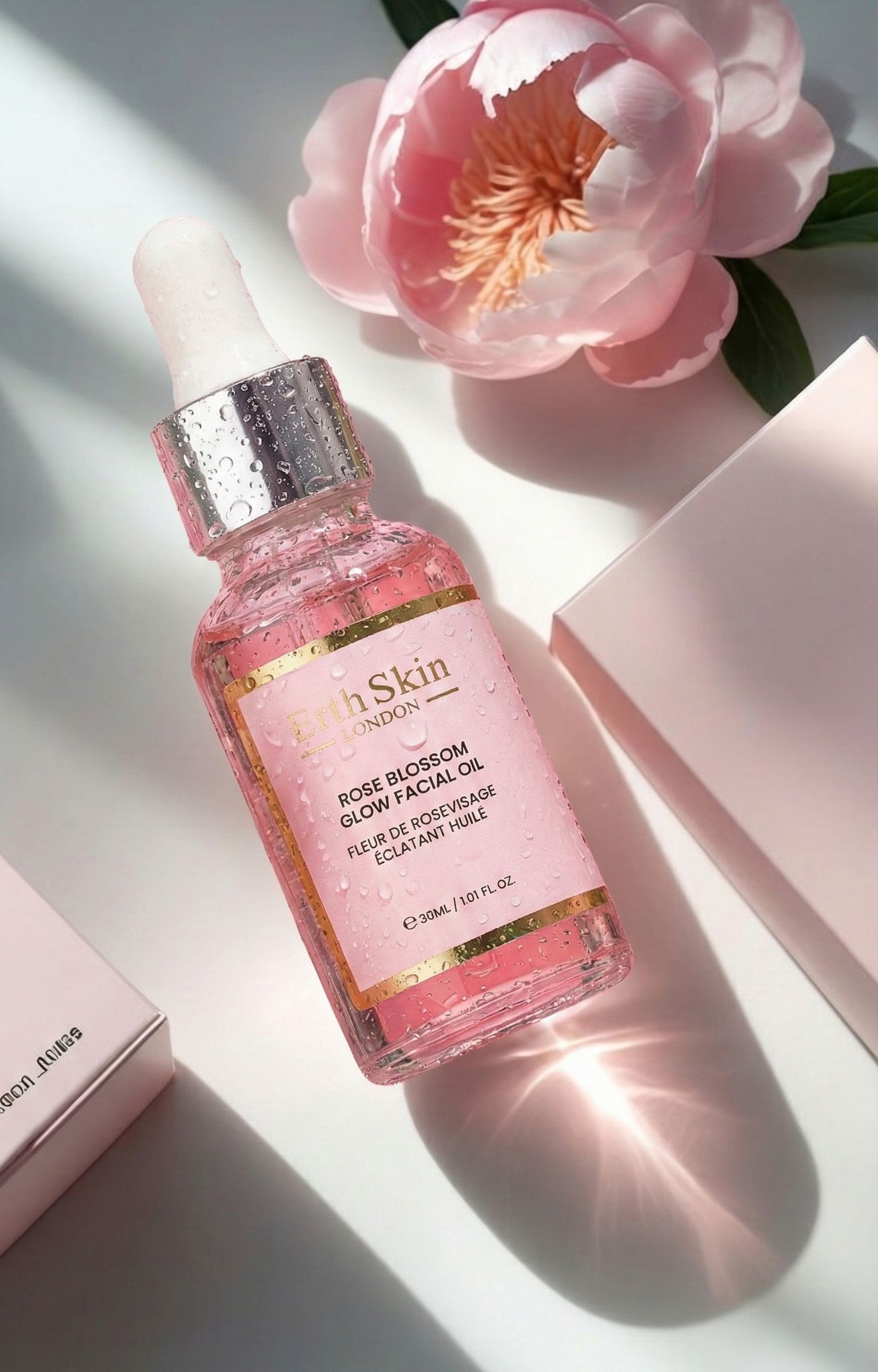 Glazen fles met druppelaar, omringd door waterdruppels en roze bloemen. Bevat roze gezichtsolie.