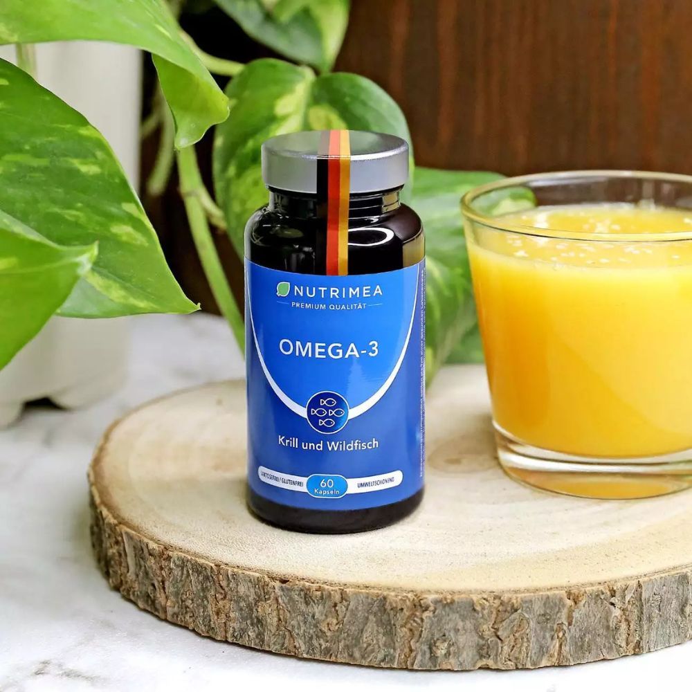 Fles Omega-3 capsules op houten plank. Glas sinaasappelsap ernaast. Groene achtergrond.