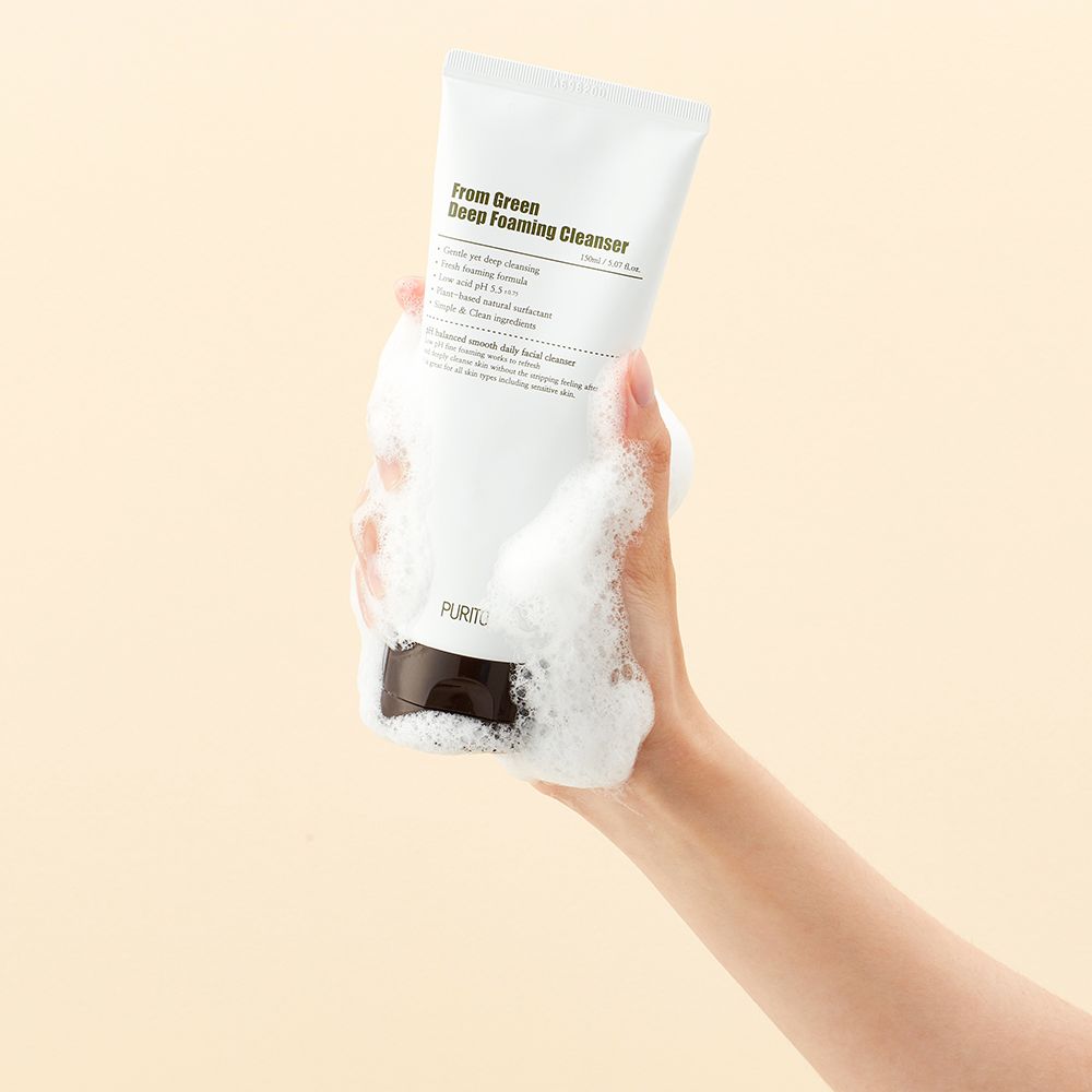 Een hand houdt een witte tube diepgroene schuimende reiniger vast met schuim.