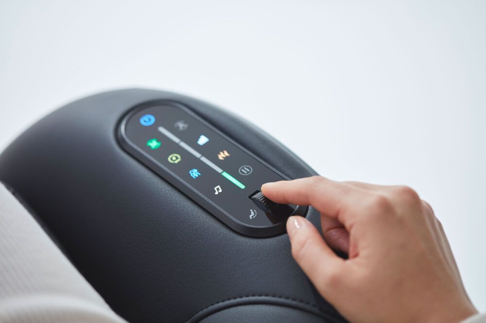 Gros plan sur l'interface de commande d'un fauteuil de massage noir. Main actionnant les commandes tactiles.