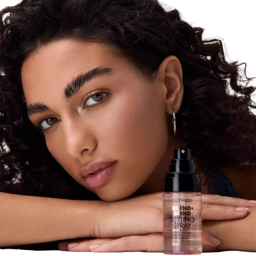 Femme aux cheveux bouclés tenant un flacon de spray. Inscription : Blend + Bond Setting Spray. Tête noire, flacon transparent.