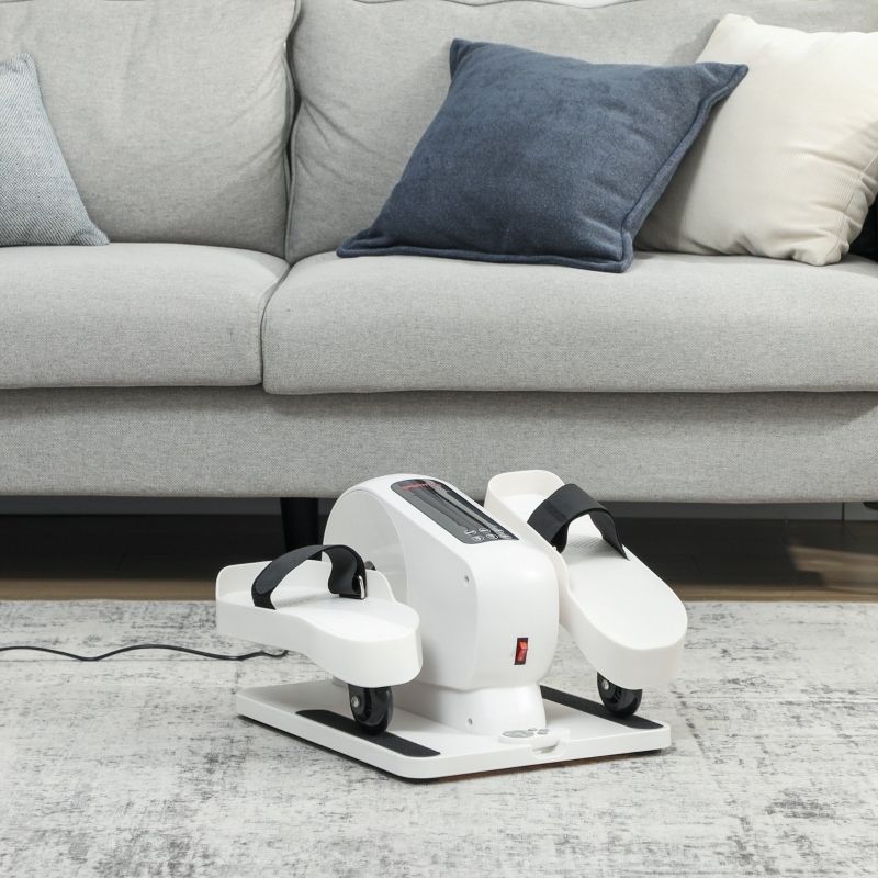 Witte mini-elliptische trainer met zwarte banden. Op tapijt voor bank. Rode aan/uit-knop, wielen.