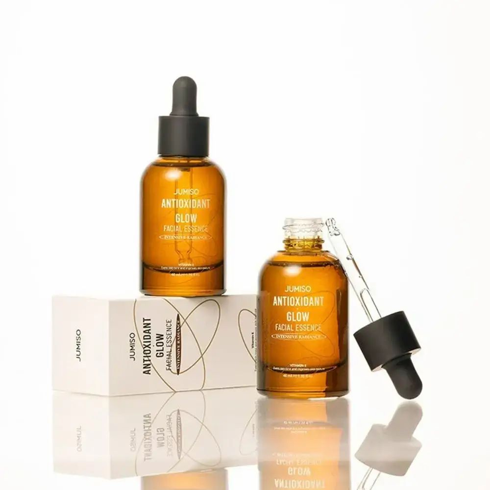 Twee bruine glazen flessen met zwarte dop en pipet. Opschrift: JUMISO ANTIOXIDANT GLOW FACIAL ESSENCE. Met verpakking.
