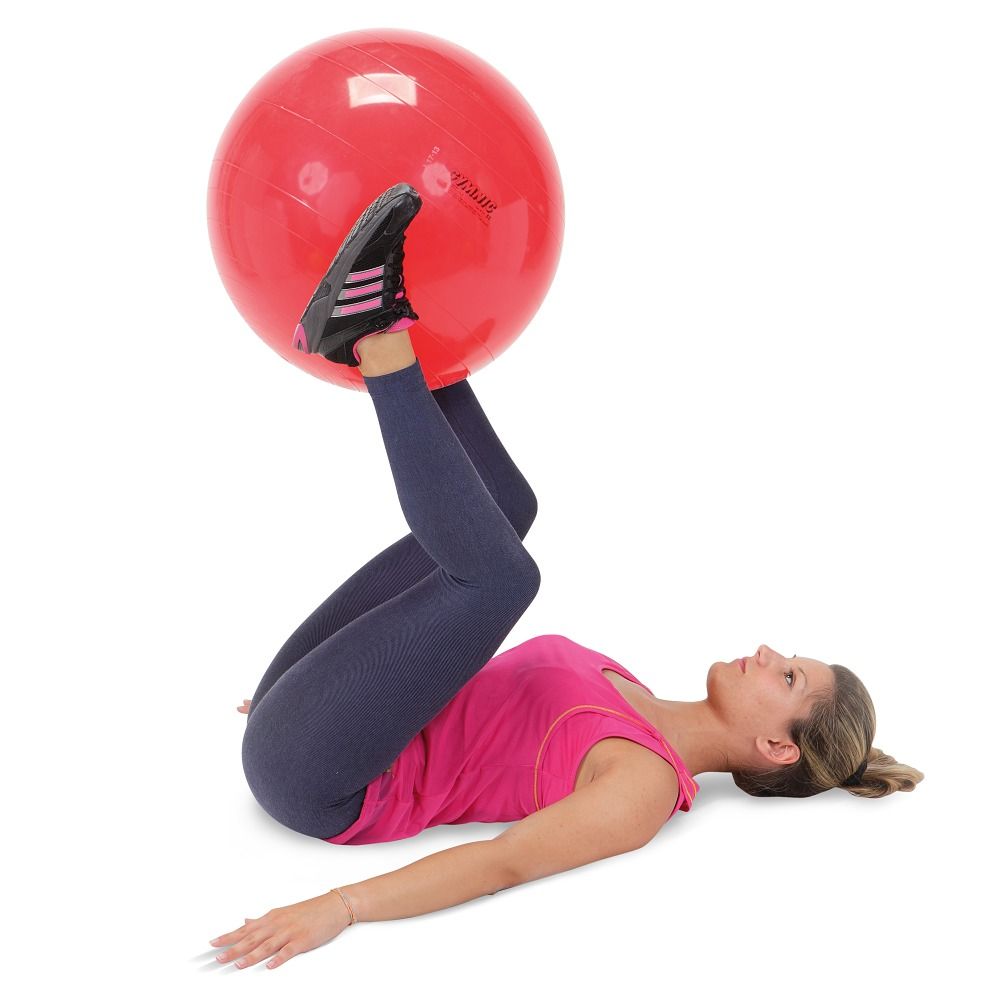 Een vrouw ligt op haar rug en houdt een rode gymnastiekbal tussen haar voeten.