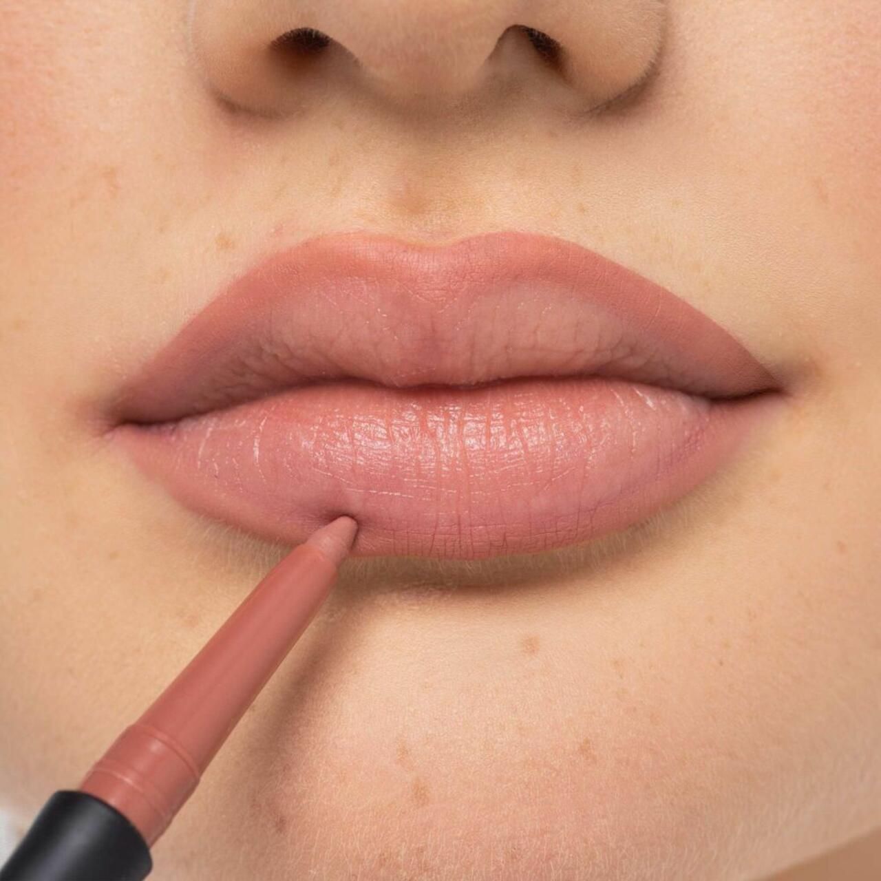 Persoon tekent lipcontour met roze lippenstift.