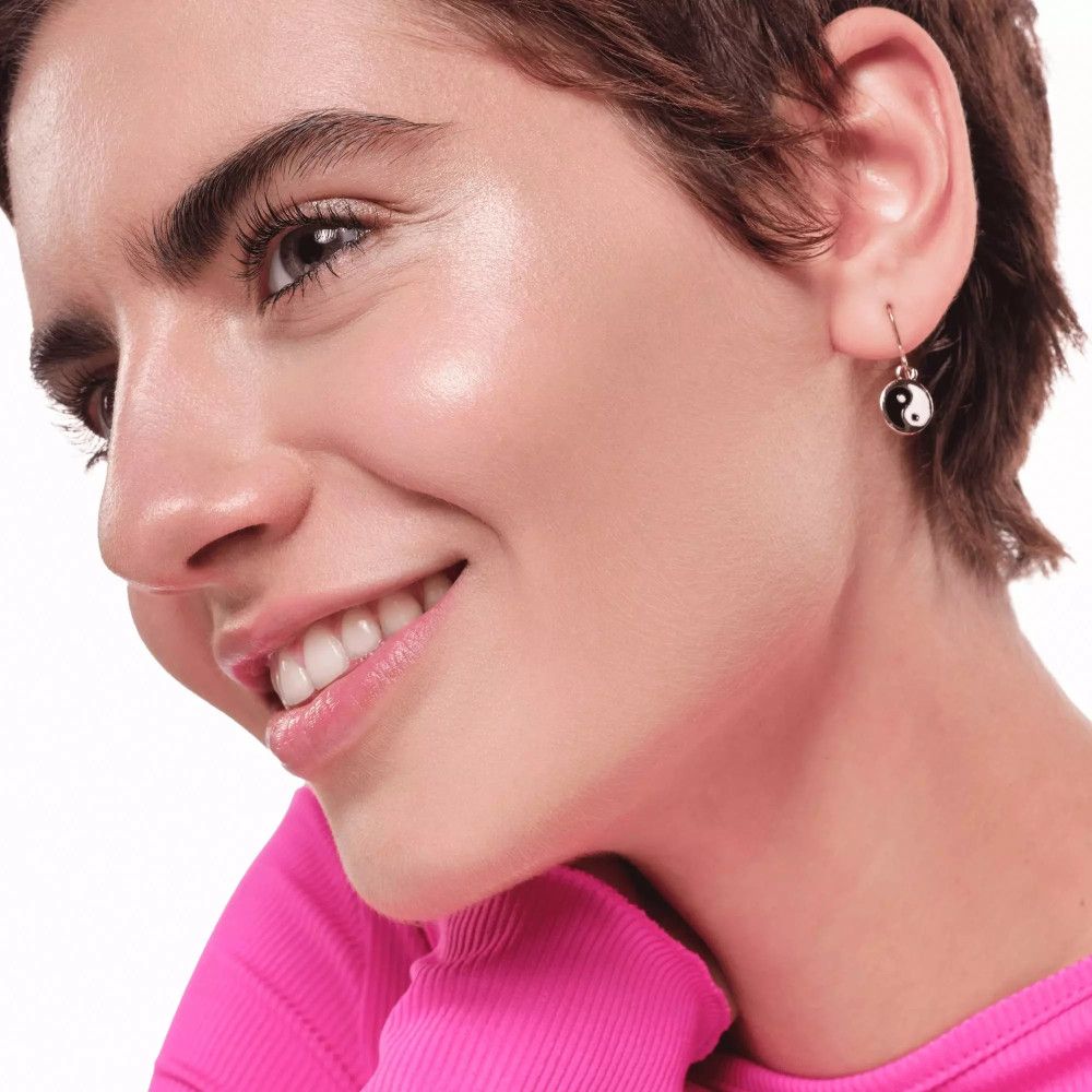 Close-up van een vrouw met Yin-Yang-oorbel. Ze lacht. Huid geaccentueerd met highlighter.