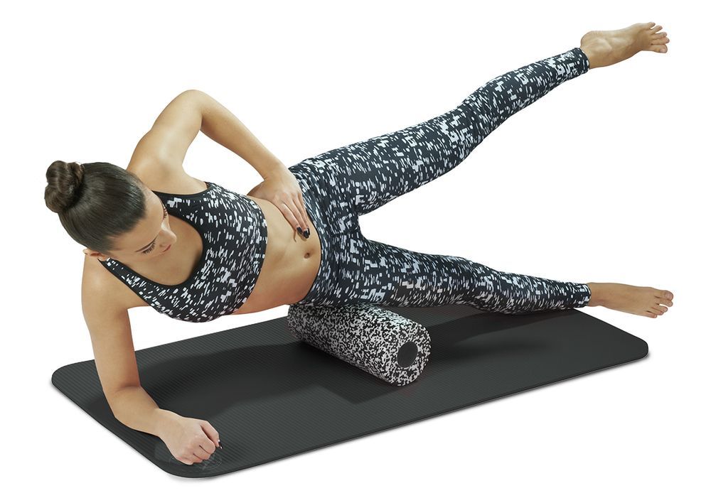 Femme sur un tapis utilisant un rouleau de fascia. Le rouleau est sous sa cuisse. Vêtements de sport.