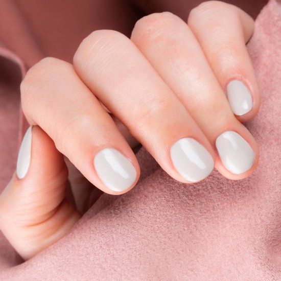 Main avec ongles vernis couleur sable. Posée sur un tissu rose.