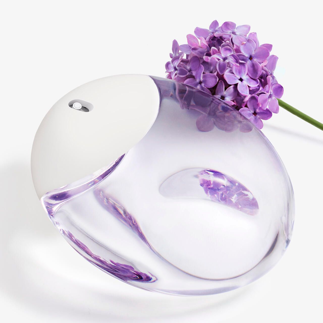 Flacon rond avec bouchon blanc, rempli de liquide violet. Fleurs violettes à côté.