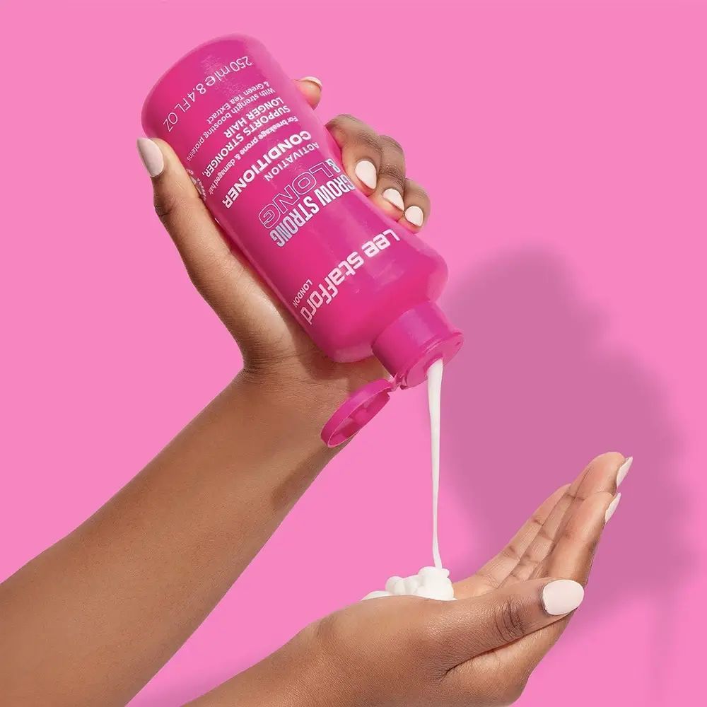 Handen houden roze fles, product wordt uitgegoten. Tekst: Grow Strong & Long Conditioner. Merk: Lee Stafford.