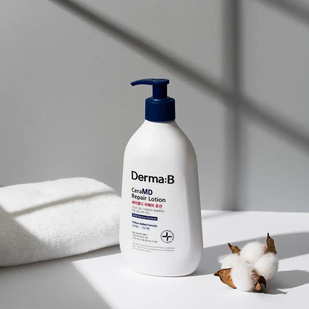 Witte fles met blauwe pomp. Opschrift: Derma:B CeraMD Repair Lotion. Naast een handdoek en katoenbloemen.