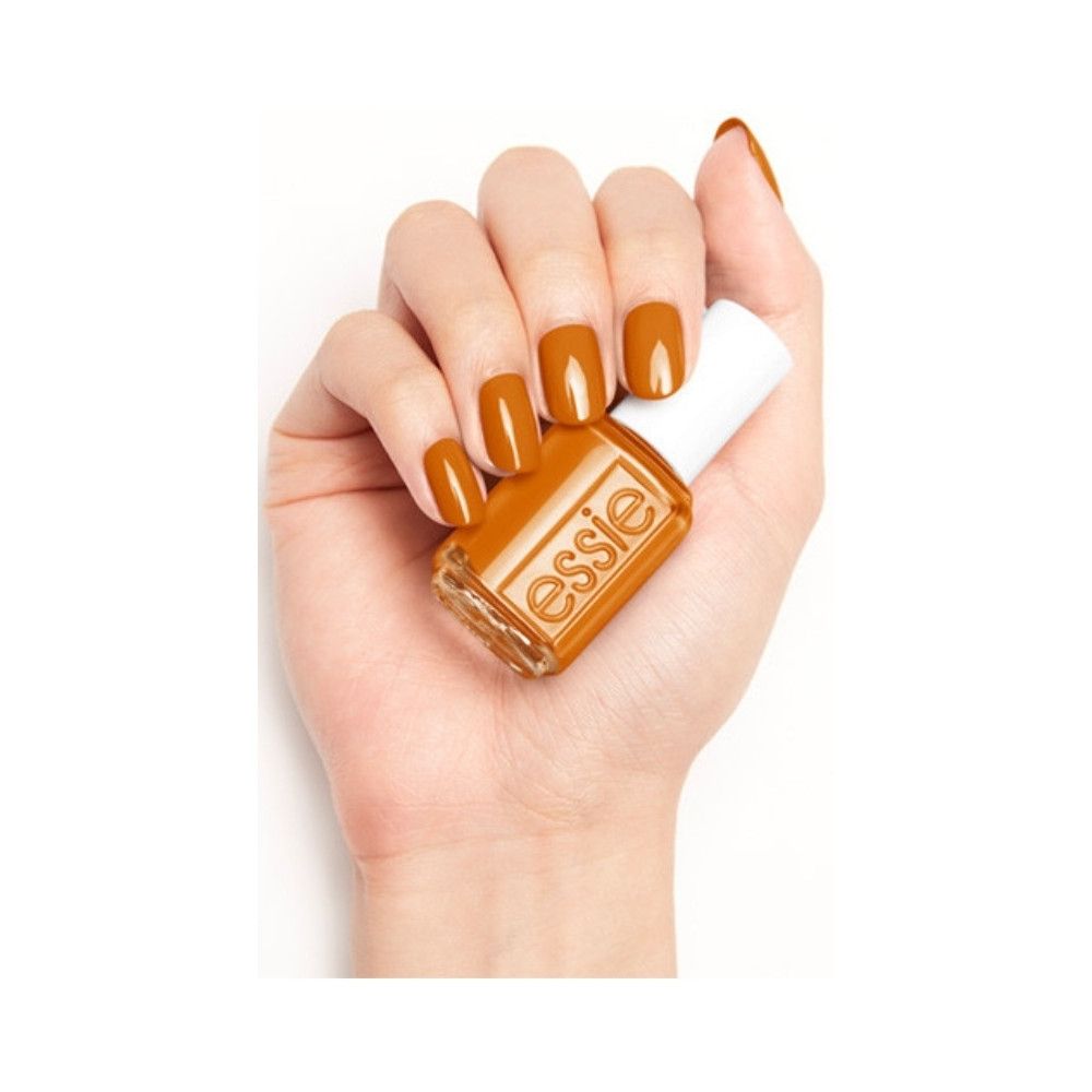 Hand met gelakte nagels en nagellakfles. Fles met witte dop, oranje lak en Essie-logo.