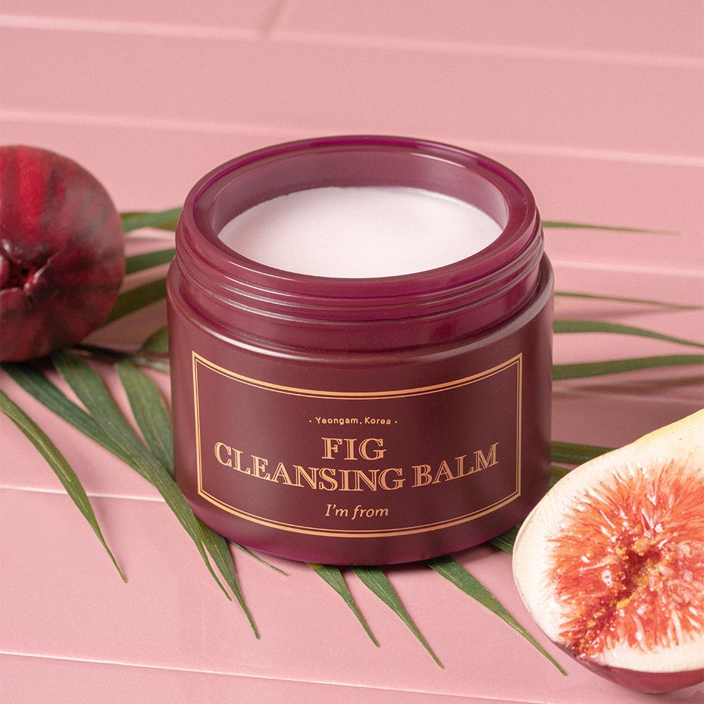 Pot ouvert avec contenu blanc, entouré de figue et feuille. Texte doré: FIG CLEANSING BALM, I'm from.