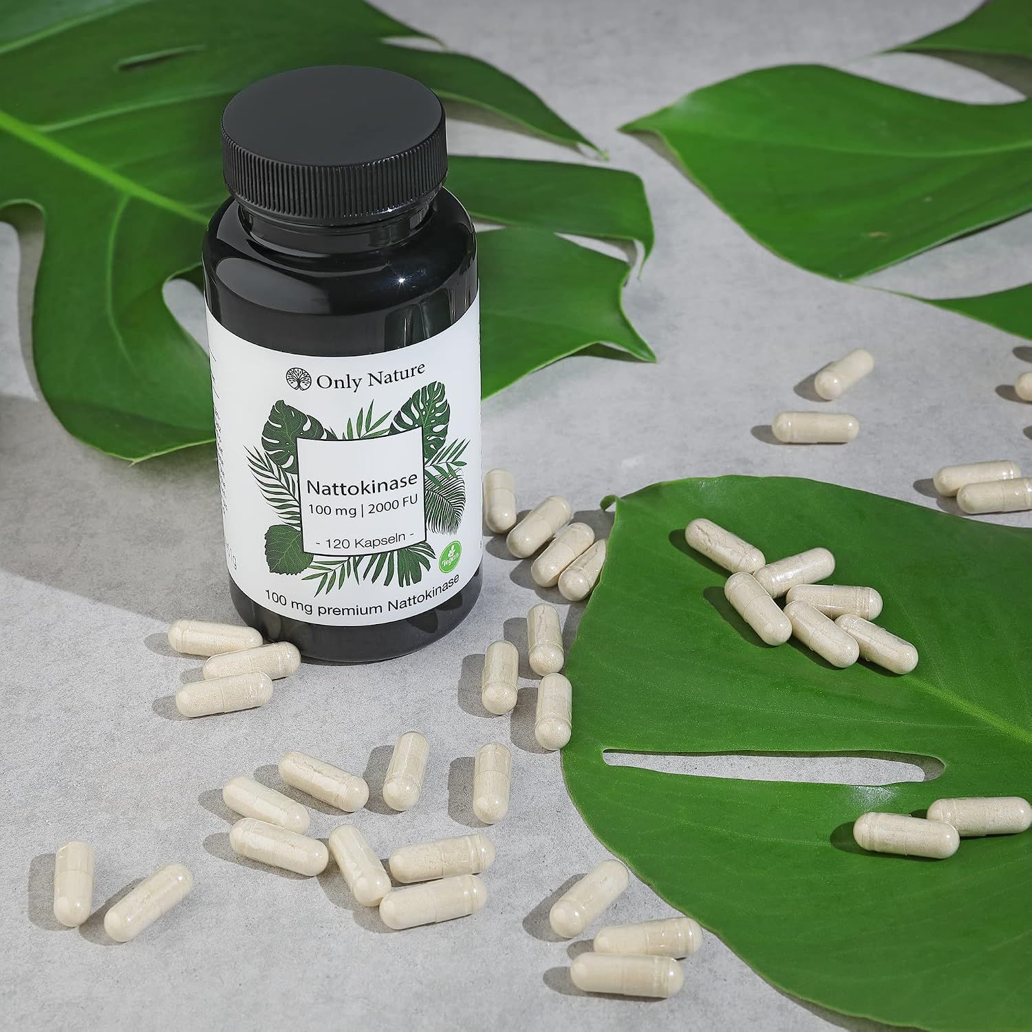 Boîte de gélules Nattokinase avec des feuilles vertes et des gélules éparpillées sur la table.