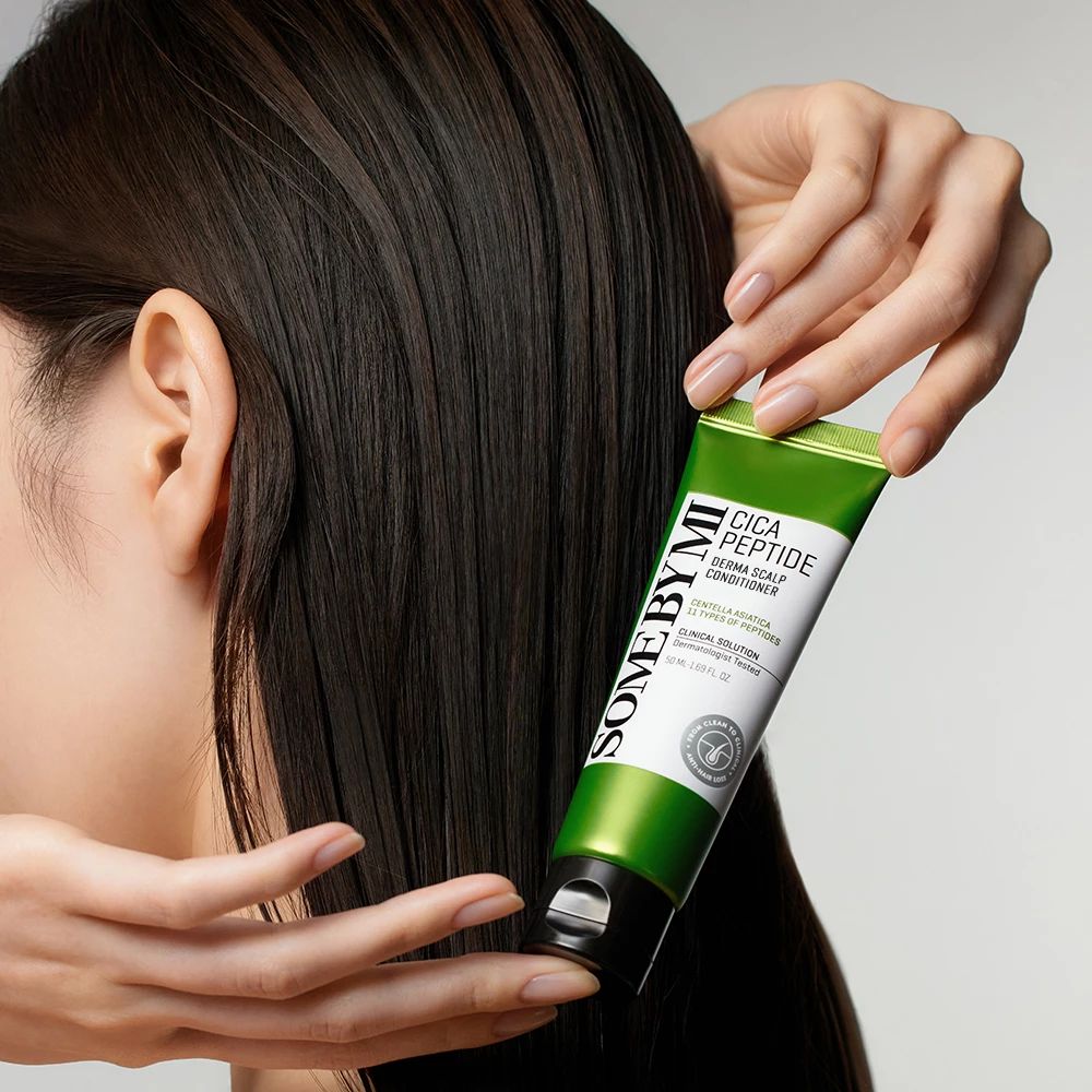 Tube verte SOME BY MI Cica Peptide. Texte en blanc. Mains tenant le tube près de cheveux noirs. Fond clair.