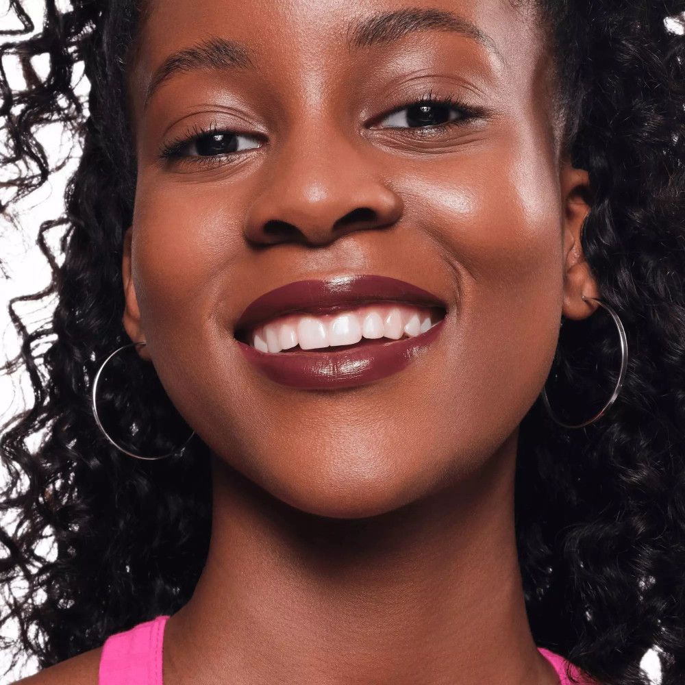 Gros plan d'un visage souriant avec du rouge à lèvres. Lèvres rouge foncé. Femme à la peau foncée et boucles d'oreilles argentées.